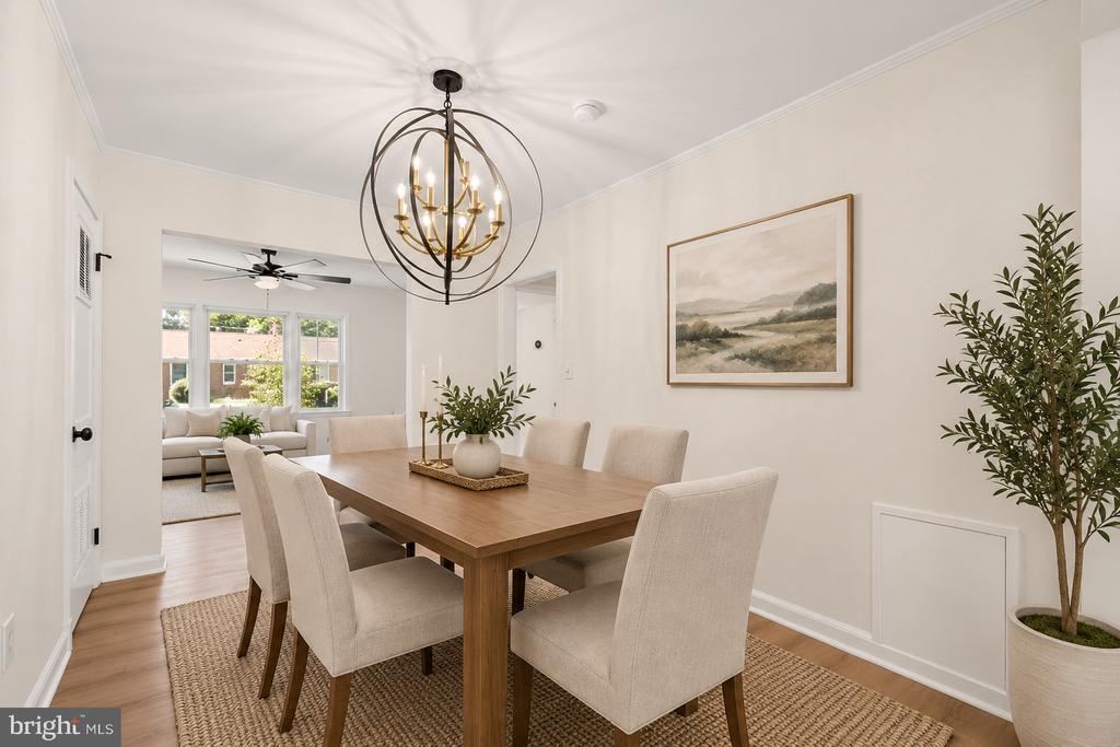 Dining room with a wood table, upholstered chairs, and a brass chandelier, opening to a bright living room.