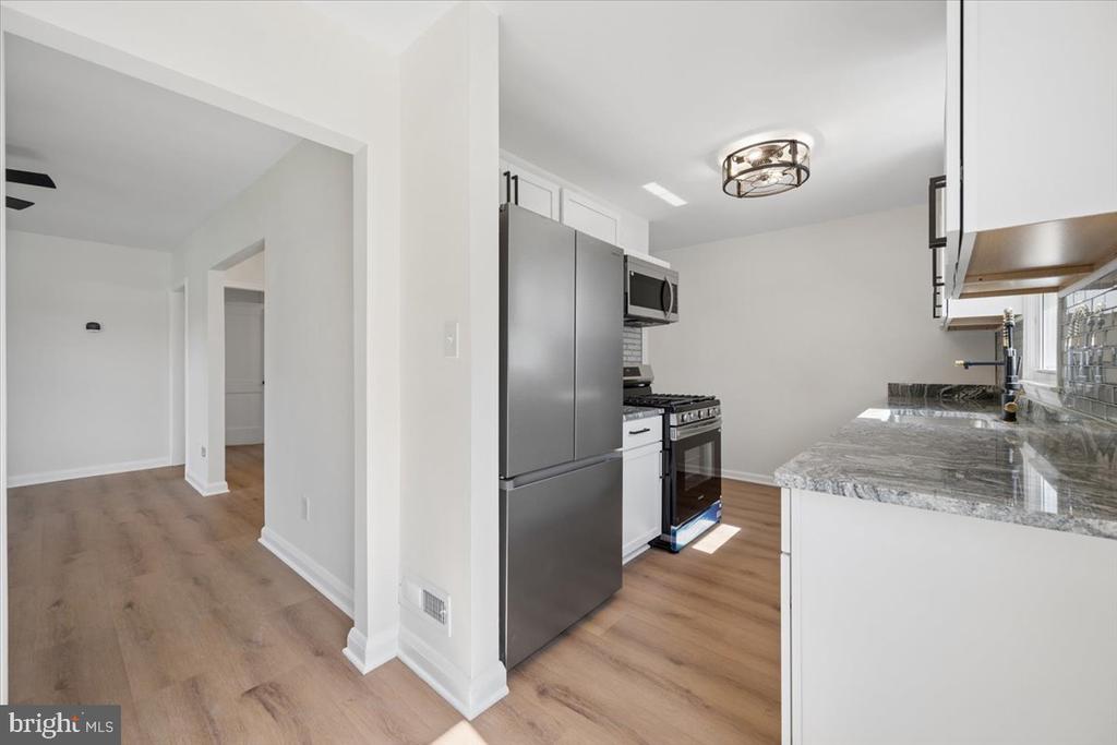 Kitchen with white cabinets, gray stone counters, stainless steel appliances, and wood-look flooring.