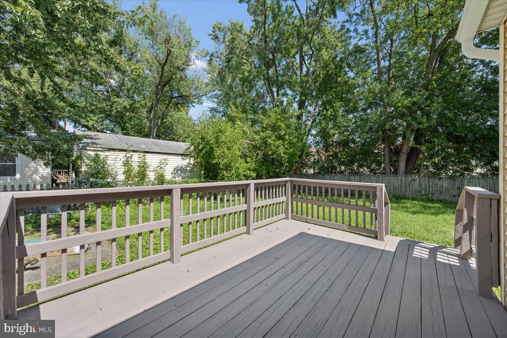 Gray deck overlooking a grassy, tree-shaded backyard enclosed by a wooden fence.
