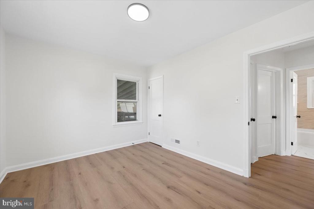 Empty room with light wood-look flooring, a window, and a doorway to a bathroom.