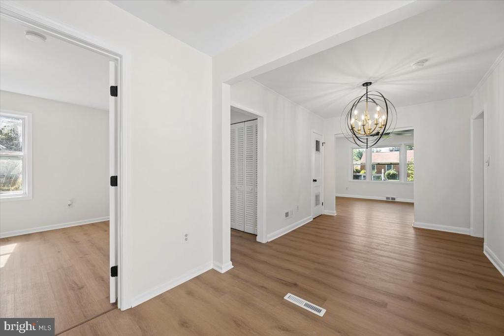 Empty dining and living area with wood floors, a globe chandelier, and large windows.