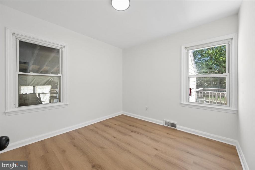 Empty room with light wood-look flooring and two windows overlooking greenery.