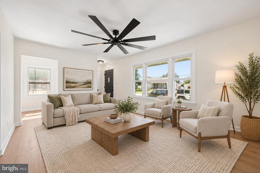 Staged living room with a beige sofa, armchairs, wood coffee table, and black ceiling fan.