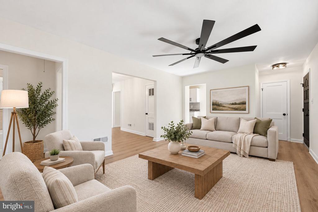 Staged living room with cream sofas, a large wood coffee table, and a black ceiling fan.