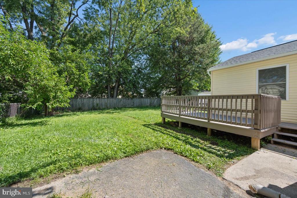 Backyard with a raised wooden deck, lawn, mature trees, and privacy fence.