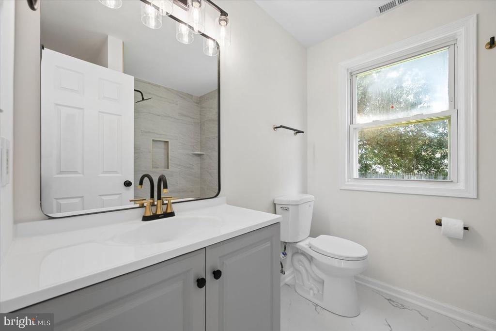Bathroom with a gray vanity, large mirror, marble-look shower surround, and window overlooking trees.