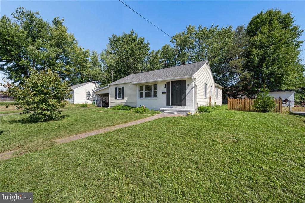 Single-story light-sided home with a dark front door, walkway, and broad lawn.