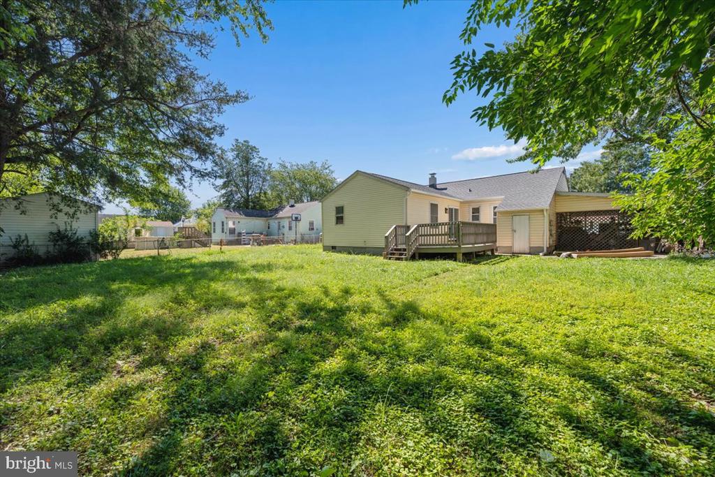 House rear and raised deck overlooking a broad grassy backyard shaded by leafy trees.