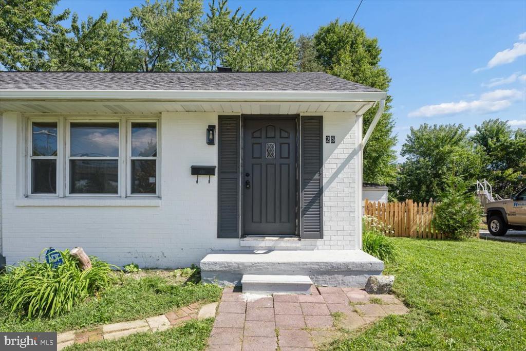 White-brick house with a dark front door, matching shutters, and a paved entry walkway.
