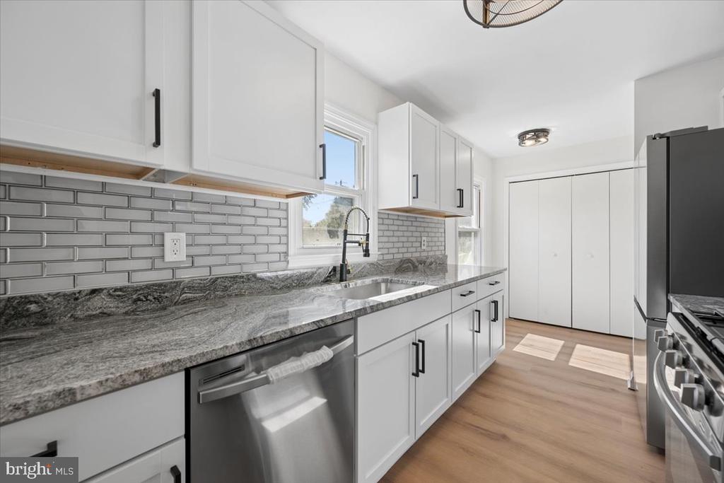 Kitchen with white cabinets, gray tile backsplash, stone counters, and stainless-steel appliances.
