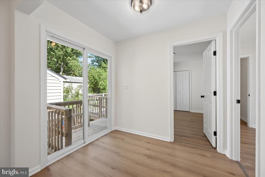 Vacant room with light wood flooring and sliding glass doors opening onto a deck.