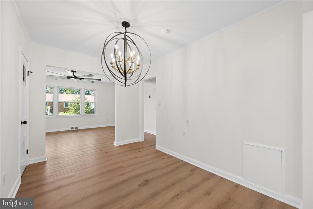 Empty dining area with a distinctive black-and-brass chandelier and light wood flooring.