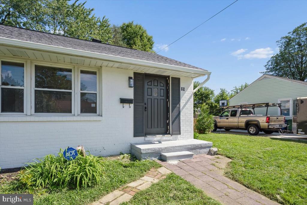Single-story white brick house with a gray front door and paved walkway.