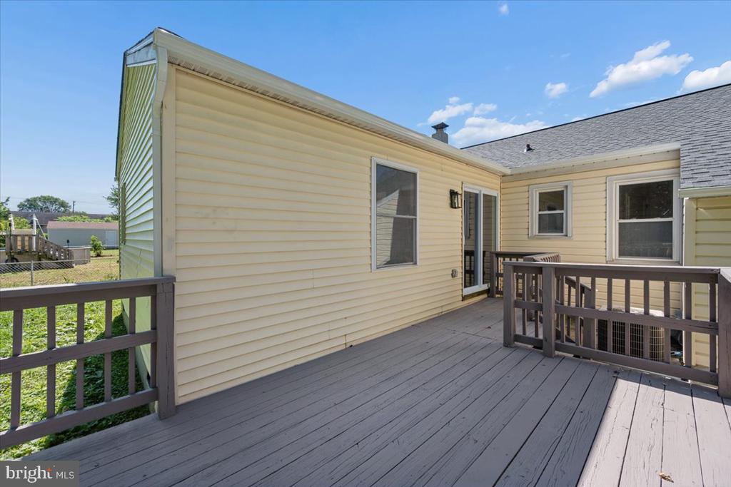 Spacious gray deck along a light yellow-sided house, with dark railings and a fenced yard.