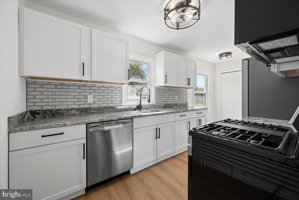 Renovated kitchen with white shaker cabinets, gray tile backsplash, stone counters, and a prominent black range.