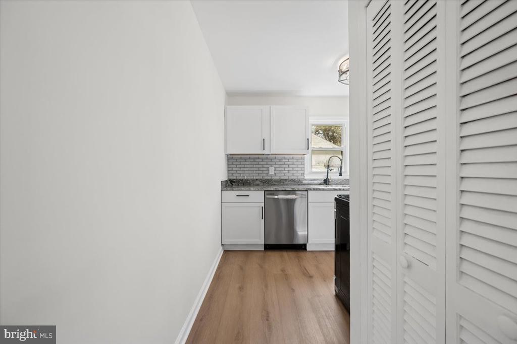 Kitchen with white cabinets, gray tile backsplash, stainless-steel dishwasher, and wood-look flooring.