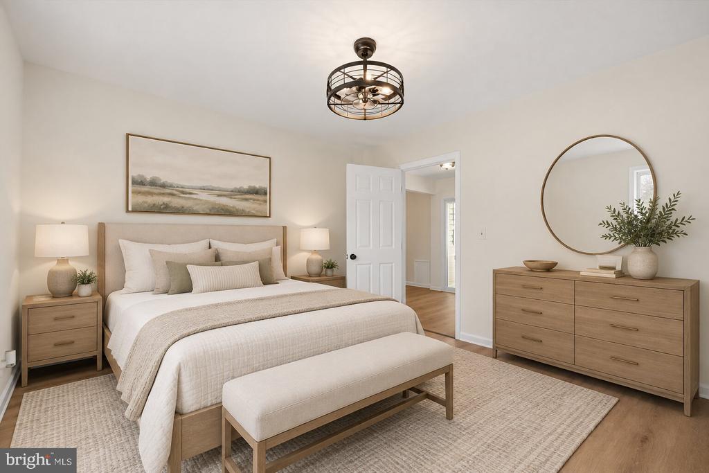 Staged bedroom with a large neutral-toned bed, matching wood furniture, and a round mirror.