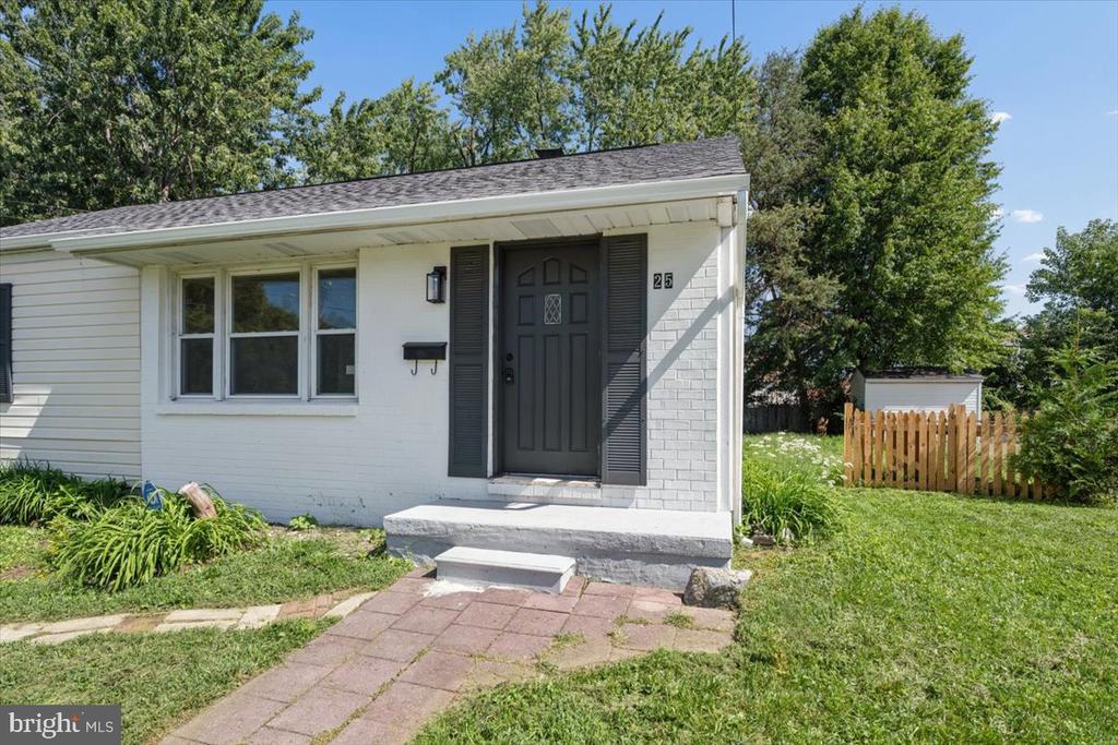White single-story home with dark shutters, a paved front walkway, and a wooden gate beside the lawn.