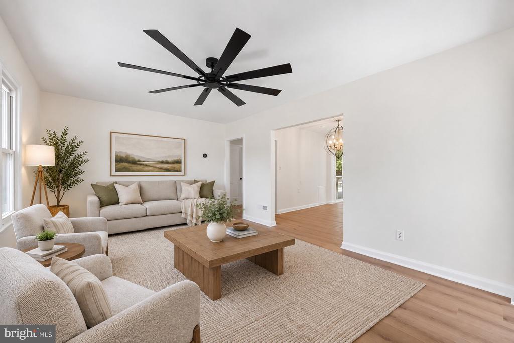 Staged living room with light sofas, a wooden coffee table, and an oversized black ceiling fan.