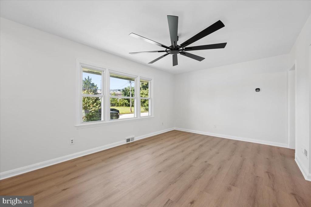 Vacant room with light wood-look flooring, a black ceiling fan, and three windows.