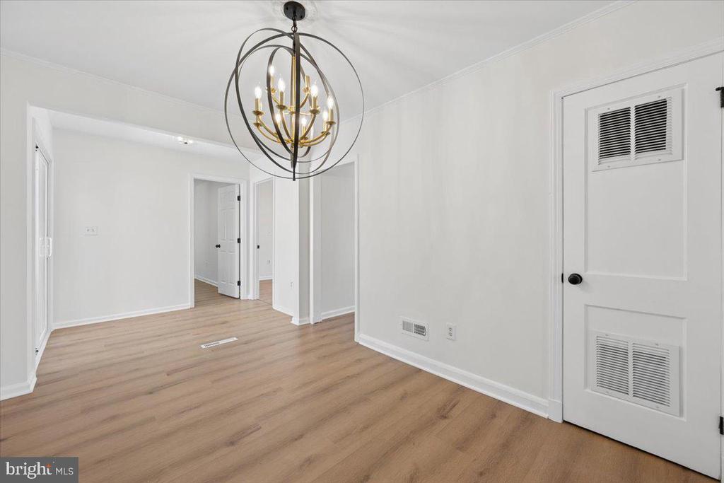 Unfurnished room with light wood floors, a globe chandelier, and a louvered utility door.