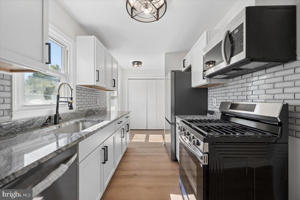 Kitchen with white cabinetry, gray stone counters, subway tile, and a dark stainless gas range.
