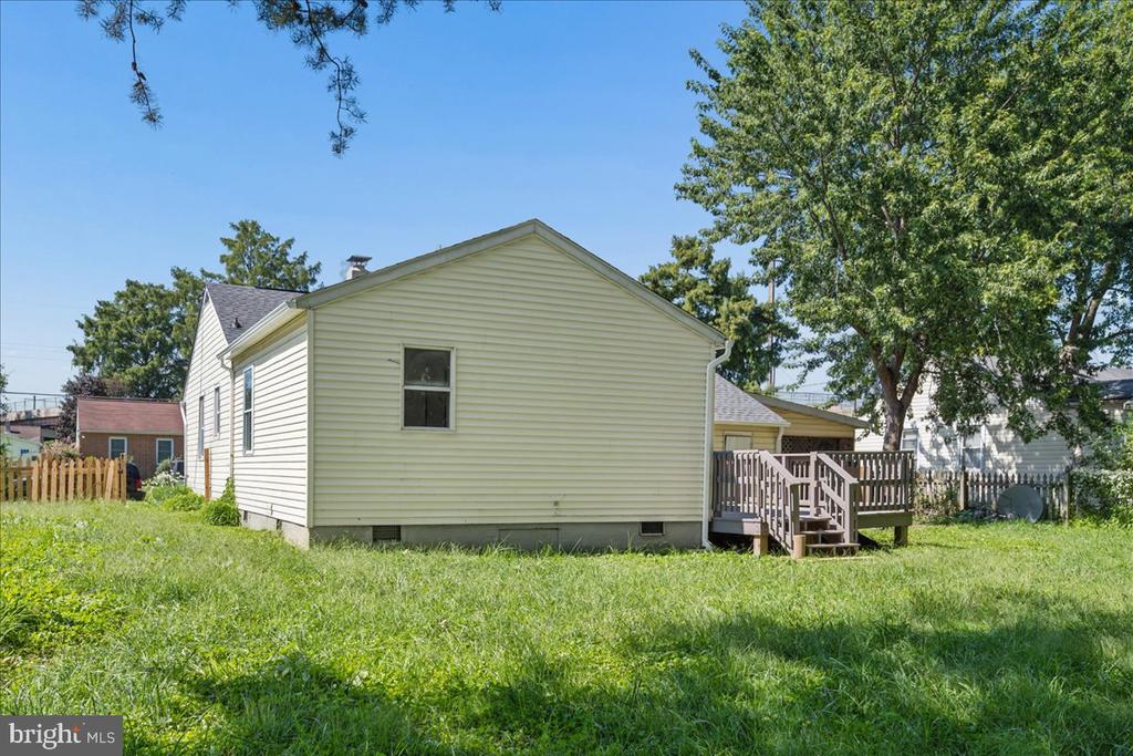 Rear of a light-colored house with a raised deck, steps, and a grassy yard.