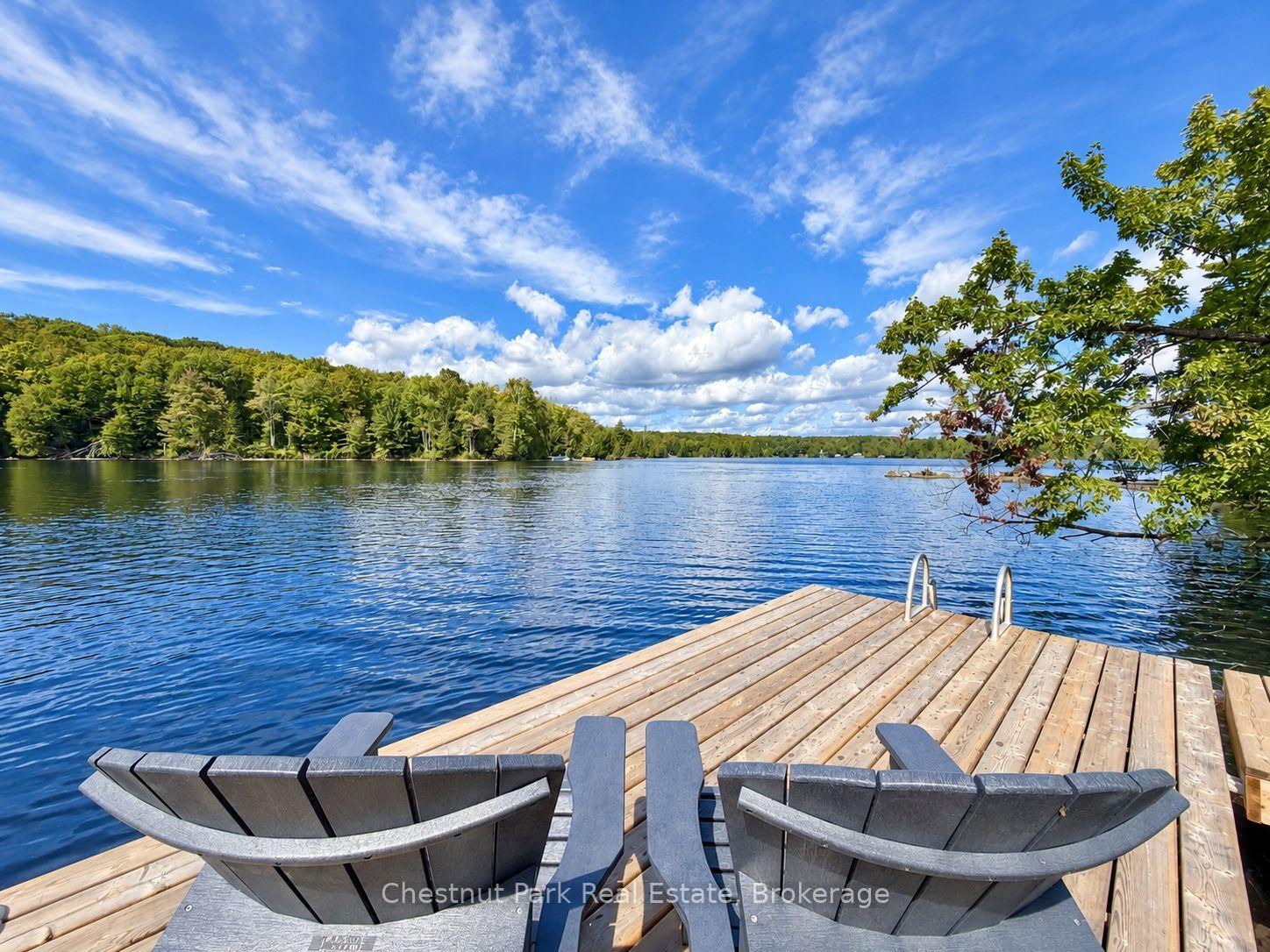 Wooden dock with Adirondack chairs overlooking a blue lake and forested shoreline.