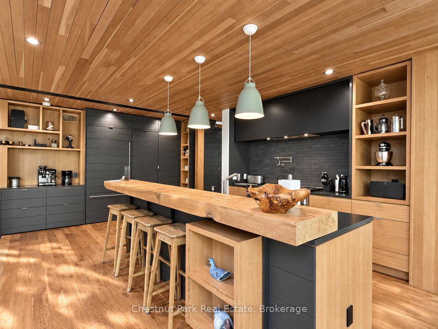Modern kitchen with a long sculptural wood island, dark cabinets, and a wood-paneled ceiling.