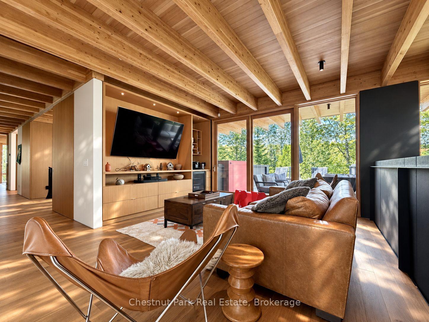 Living room with exposed wood beams, leather seating, built-in media cabinetry, and a dark fireplace.