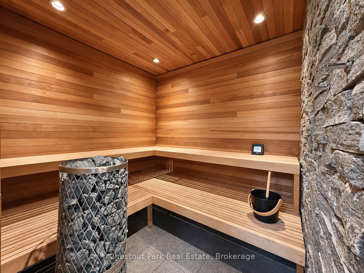 Wood-lined sauna with tiered benches, a stone wall, and a rock-filled heater basket.