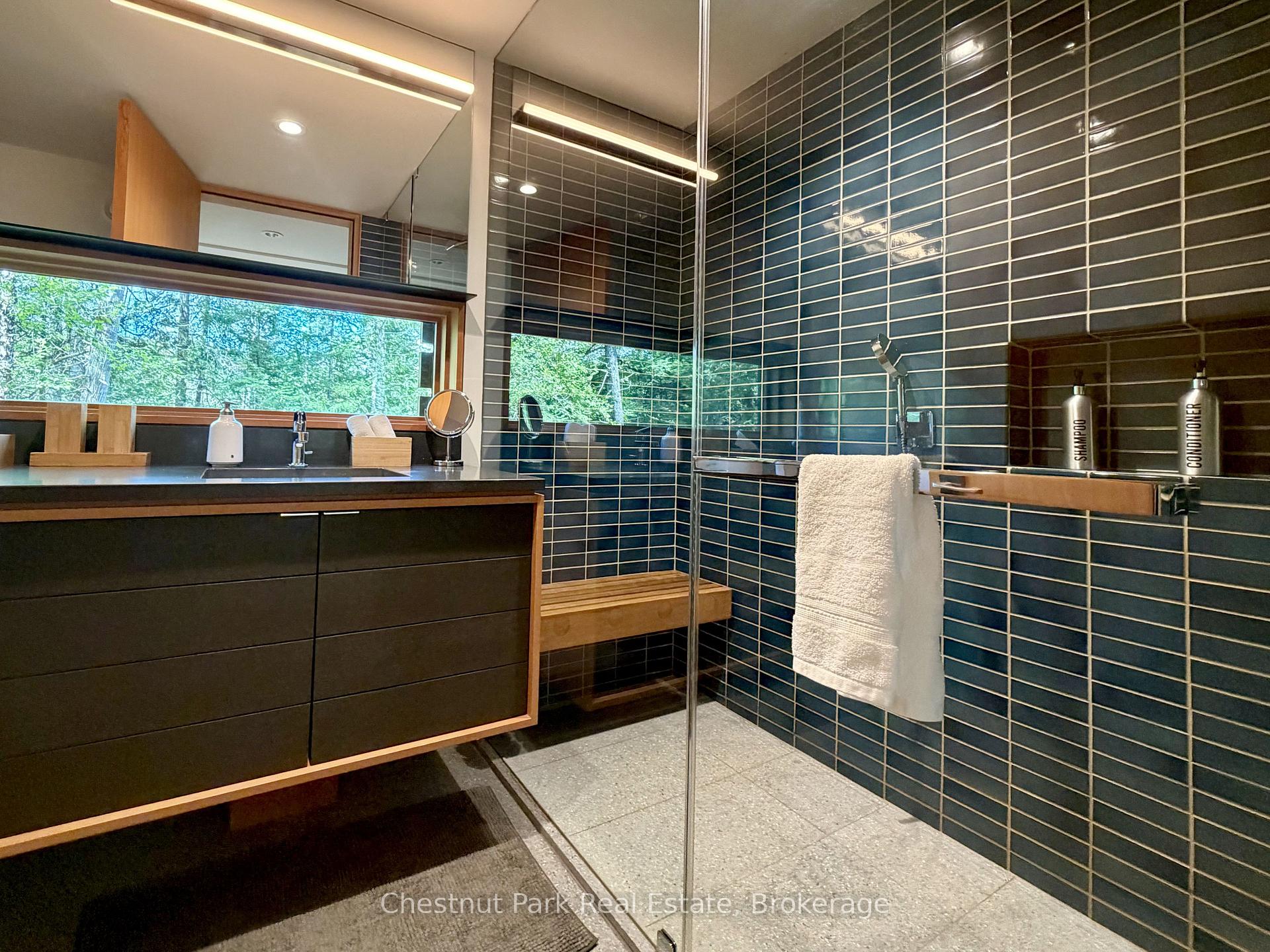 Modern bathroom with dark tiled glass shower, floating vanity, and a window overlooking trees.
