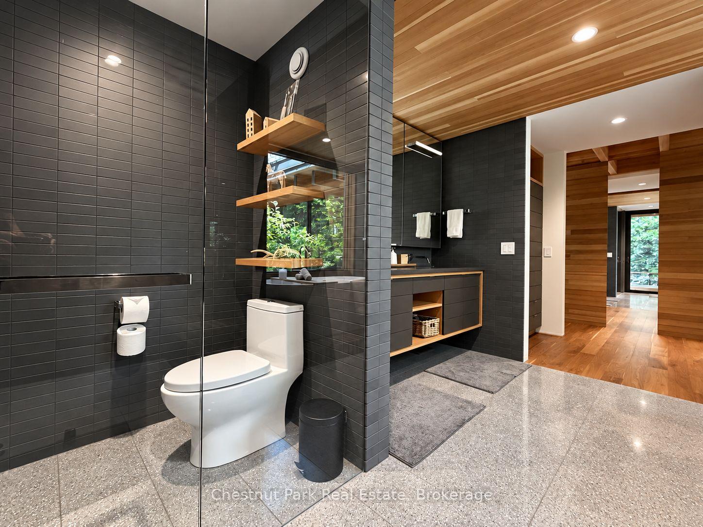 Modern bathroom with charcoal tile, glass shower, floating vanity, and warm wood ceiling.