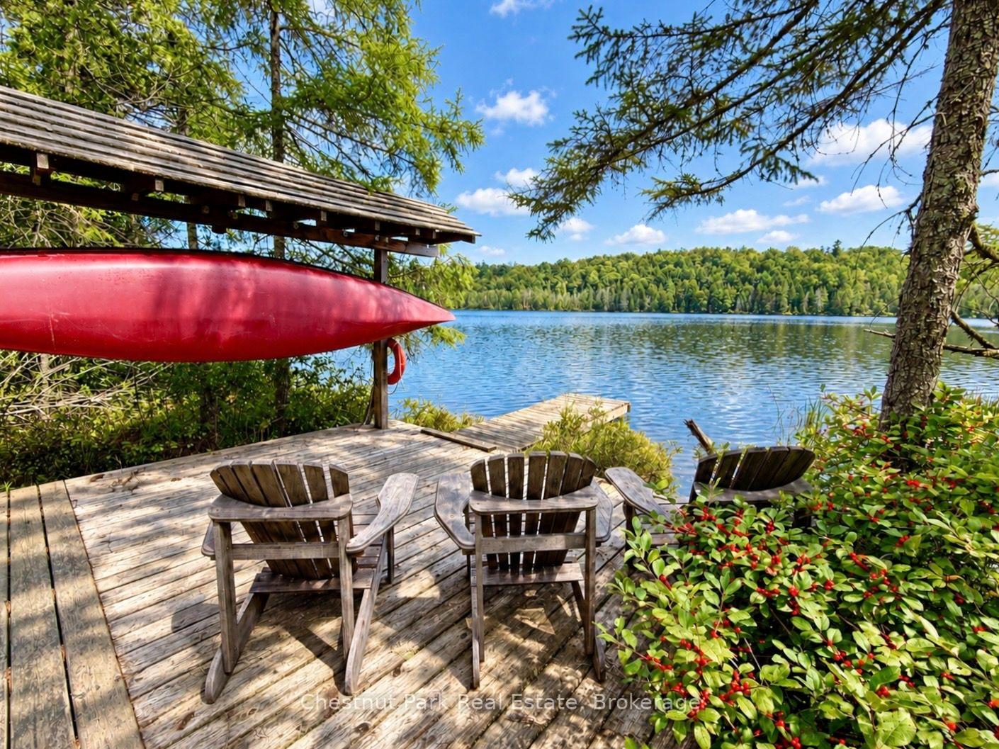 Lakeside deck with Adirondack chairs and a red canoe overlooking calm water and a forested shore.