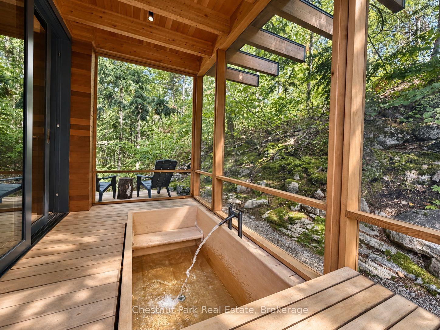 Covered wooden deck with a built-in soaking tub overlooking a lush, rocky woodland.