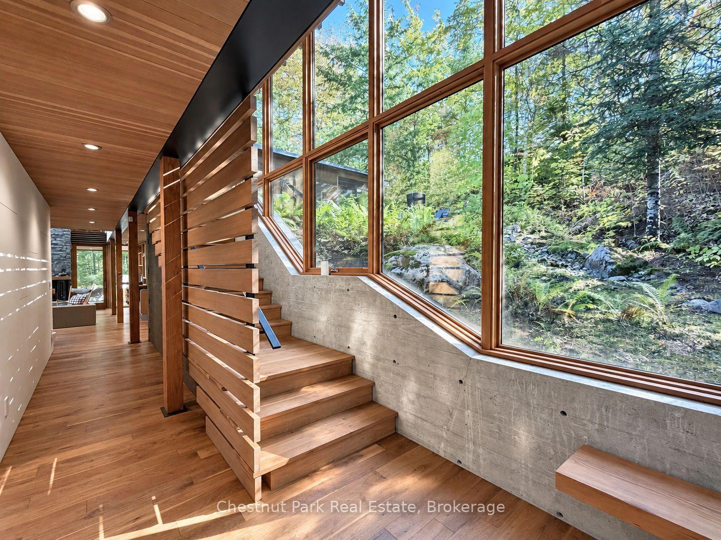 Wooden staircase and hallway beside tall windows overlooking a leafy garden.