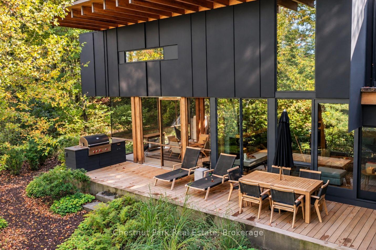Modern home with a furnished wooden deck, barbecue, and surrounding autumn foliage.