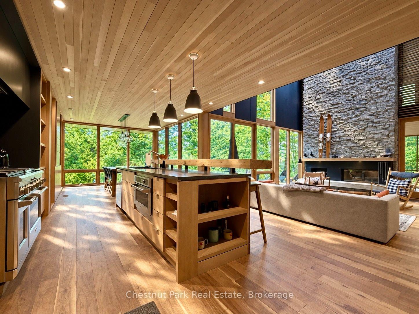 Open-plan kitchen and living room with a wood island, floor-to-ceiling windows, and a stone fireplace.
