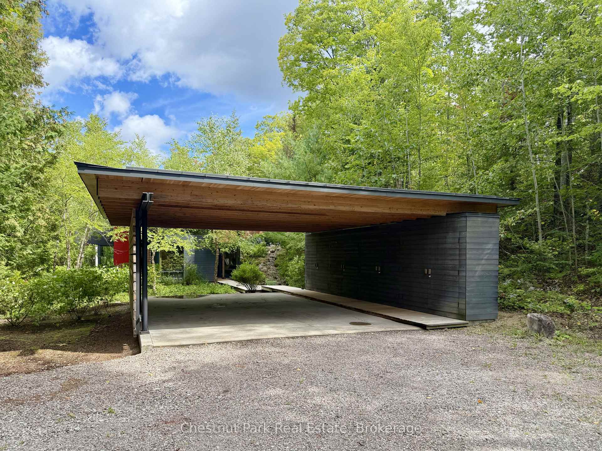 Modern wooded home with a broad wood-soffit roof sheltering a concrete carport.