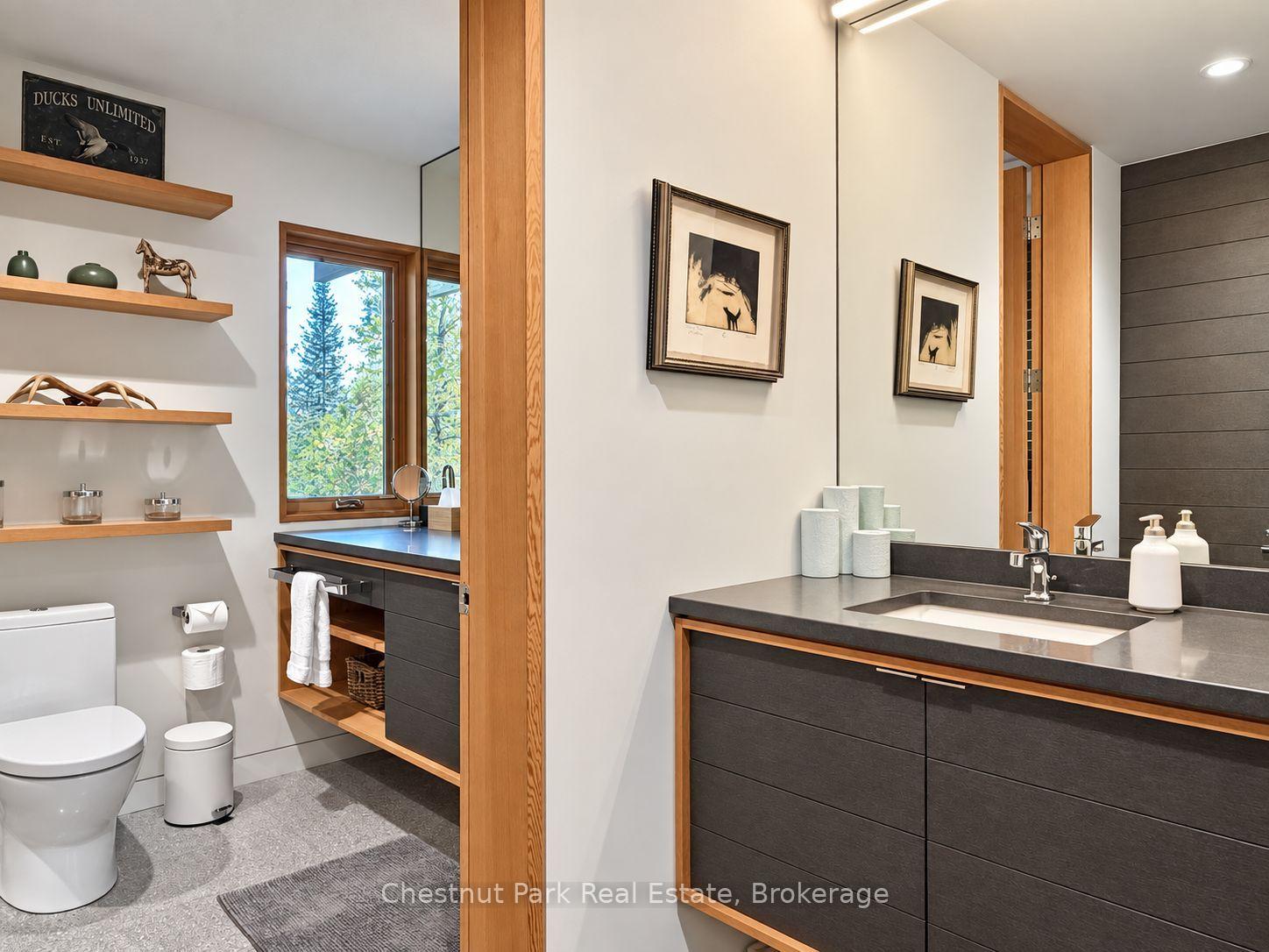Modern bathroom with dark wood vanities, warm wood trim, and a window overlooking trees.