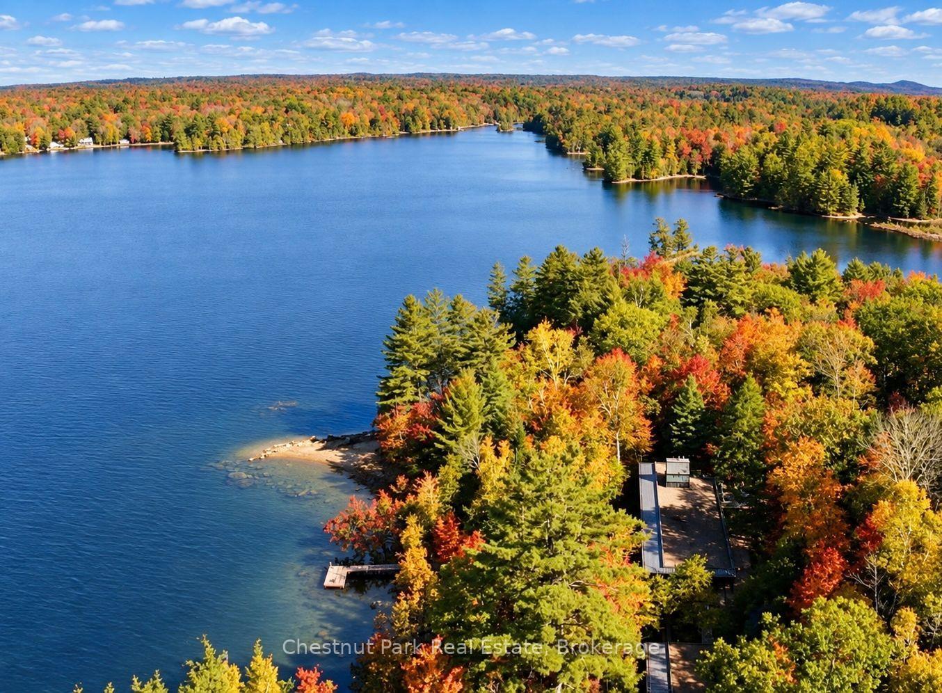 Aerial lake view with autumn-colored forest, wooded shoreline, and a dock.