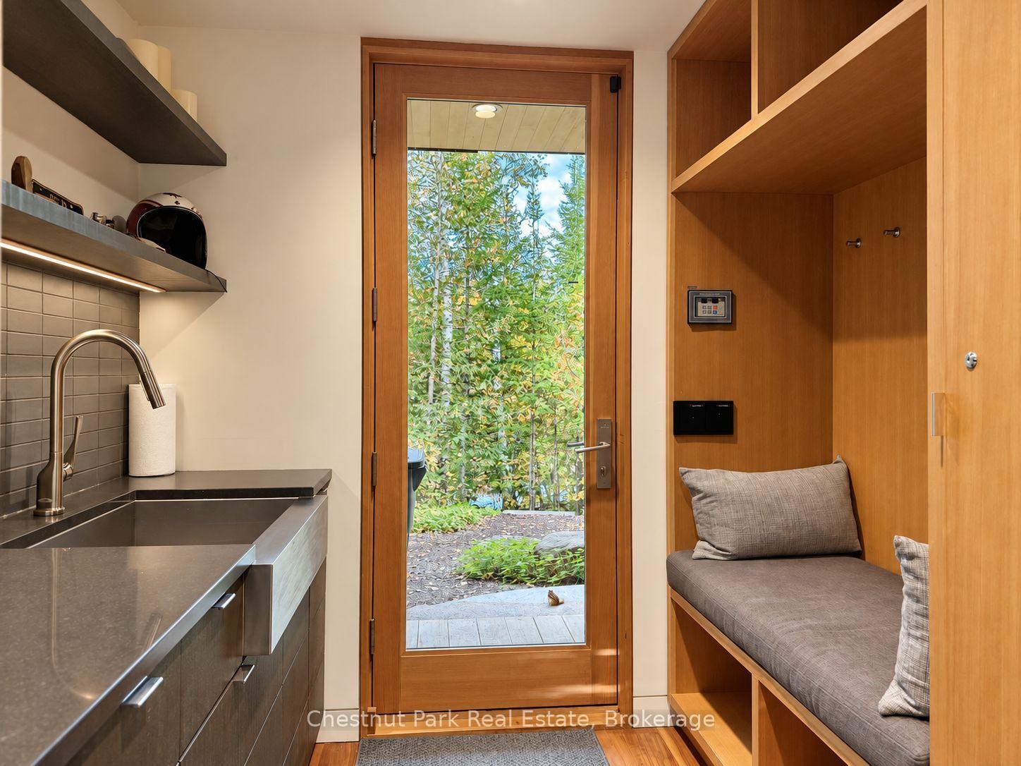 Mudroom with a built-in cushioned bench, stainless-steel sink, and glass door to a leafy garden.