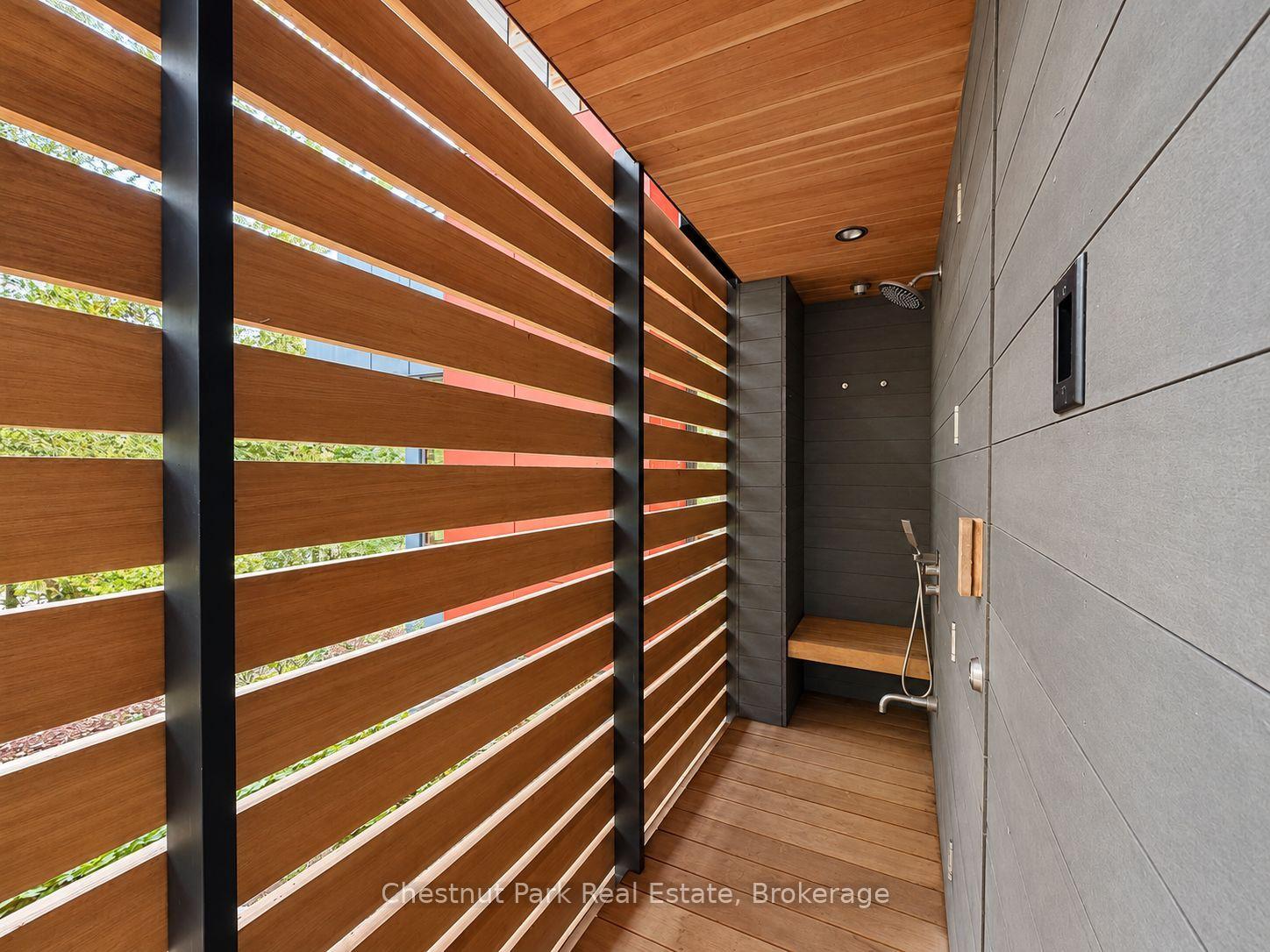 Outdoor shower with a wood slat privacy screen, wood ceiling and floor, and dark tiled walls.