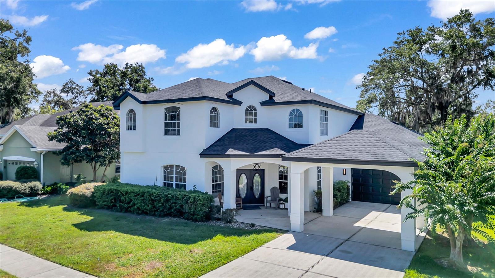 Two-story white home with arched windows, dark double doors, and a covered garage.