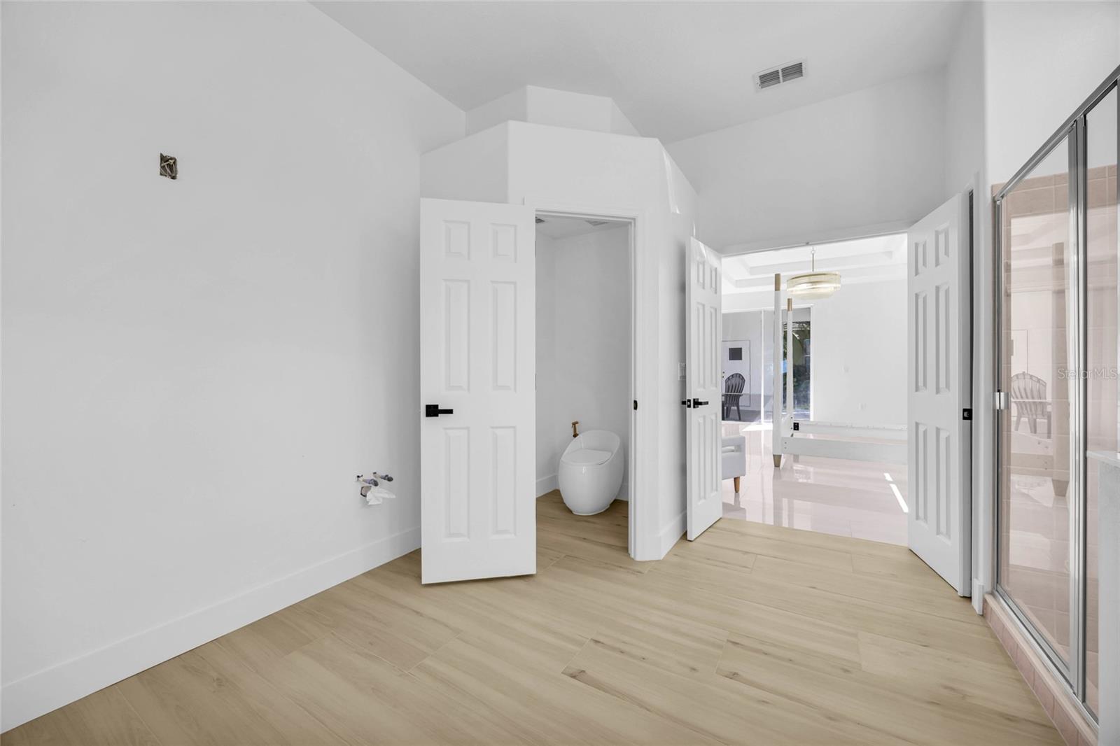 Vacant bathroom with glass shower doors, light wood-look flooring, and exposed plumbing connections.