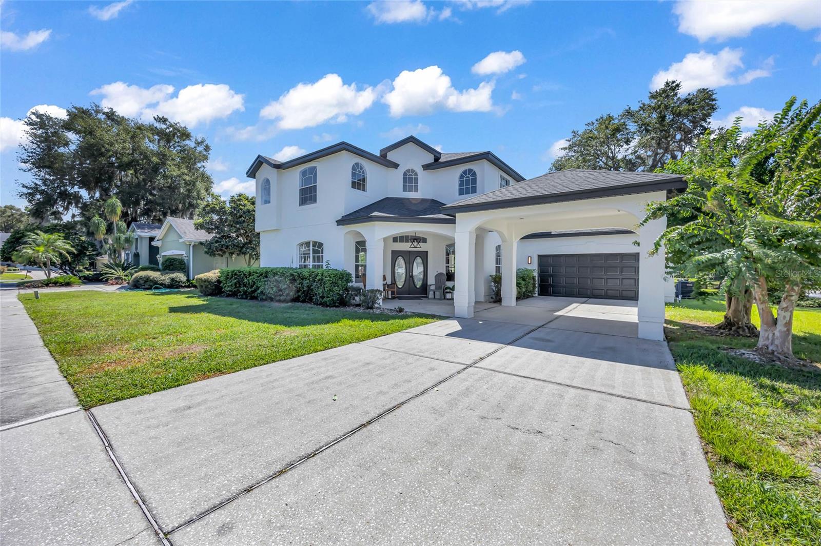 Two-story white house with arched windows, covered entry, attached garage, and broad concrete driveway.
