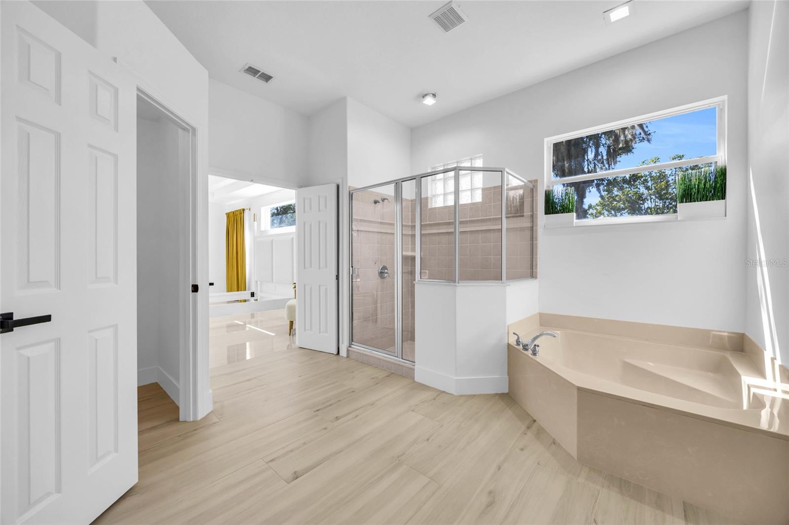 Bright bathroom with a glass-enclosed shower, built-in soaking tub, and wide window overlooking trees.