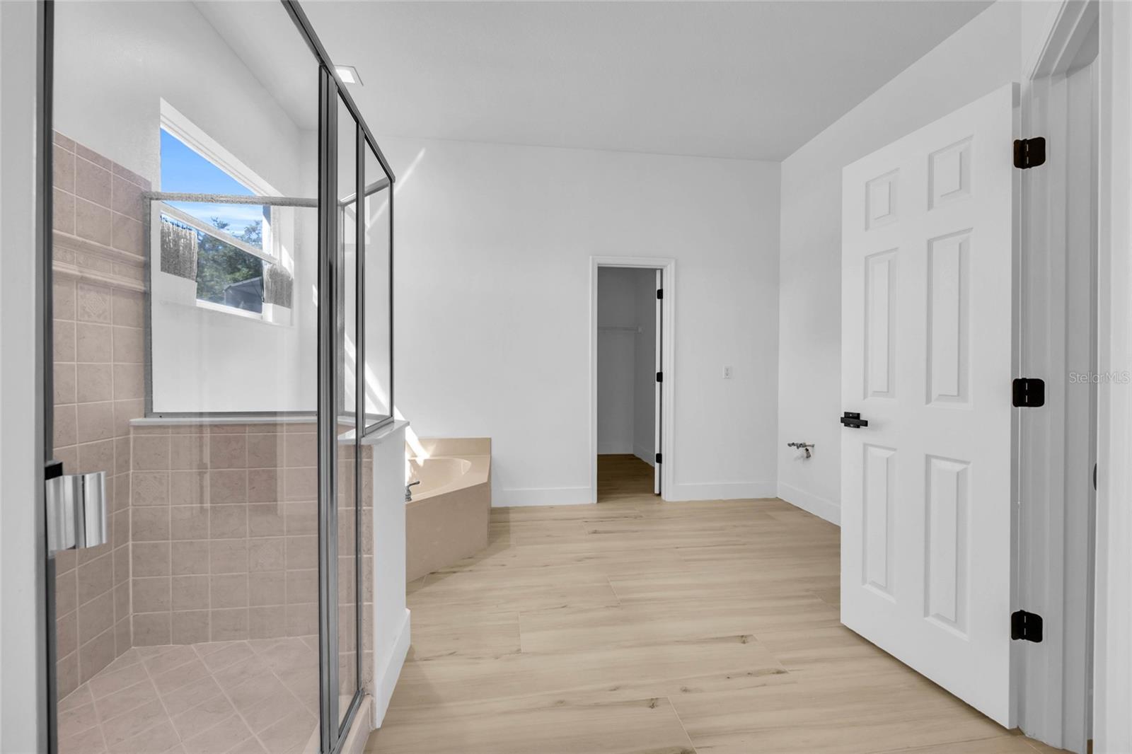 Vacant bathroom with a glass-enclosed tiled shower, corner soaking tub, and light wood-look flooring.