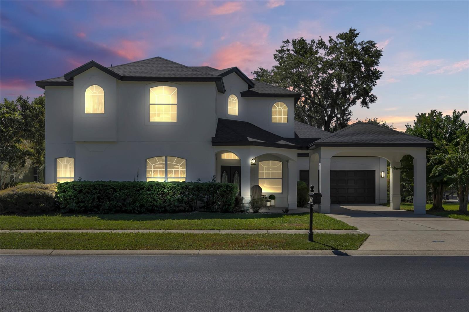 Two-story white house with glowing arched windows and an attached garage at dusk.