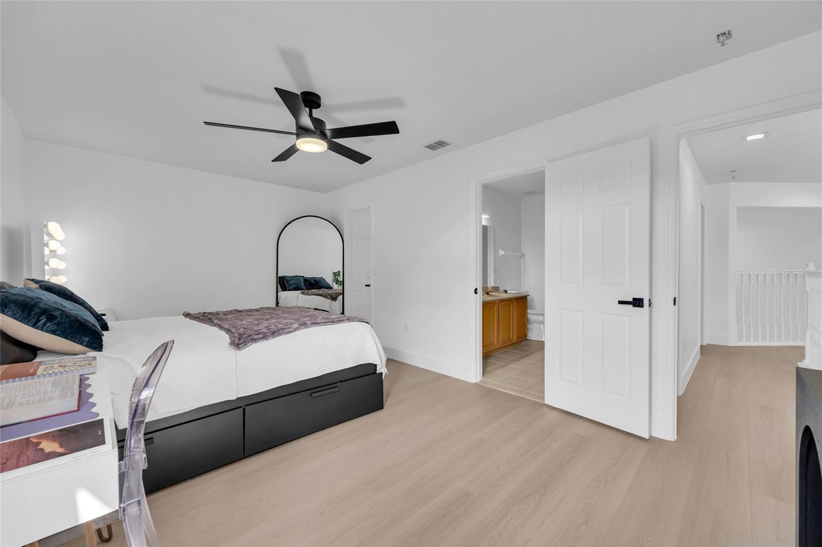 Furnished bedroom with a black ceiling fan, arched mirror, and open ensuite bathroom door.